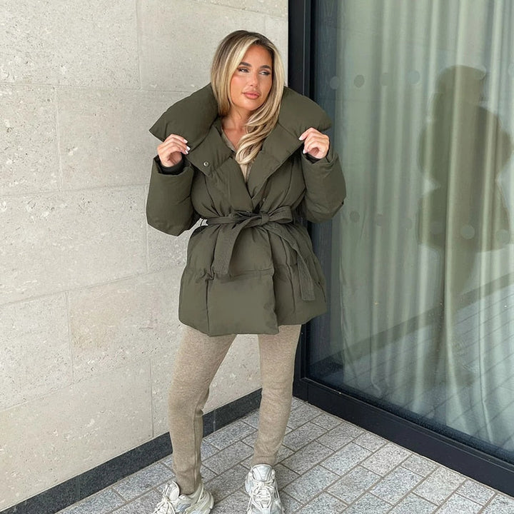 Frau in olivgrüner Daunenjacke mit Gürtel, beige Leggings, weiße Sneaker, Herbstmode.