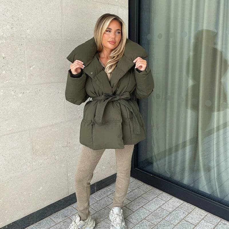 Frau in olivgrüner Daunenjacke mit Gürtel, beige Leggings, weiße Sneaker, Herbstmode.
