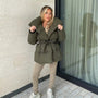 Frau in olivgrüner Daunenjacke mit Gürtel, beige Leggings, weiße Sneaker, Herbstmode.