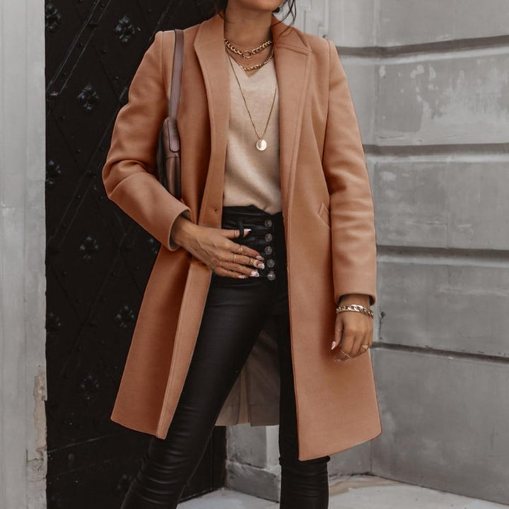 Frau in braunem Wollmantel, schwarze Lederhose, goldene Accessoires, modisch, elegant.