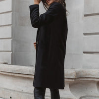 Frau in schwarzem Wollmantel, elegant, urbaner Stil, Herbstmode, vor grauer Steinwand.