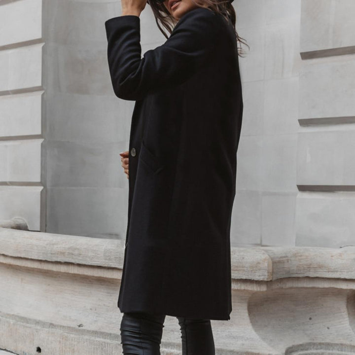 Frau in schwarzem Wollmantel, elegant, urbaner Stil, Herbstmode, vor grauer Steinwand.