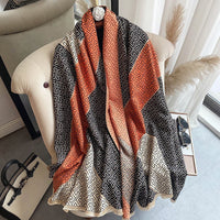 Luxuriöser Schal mit geometrischem Muster in Orange, Schwarz und Beige auf einem Sessel drapiert.