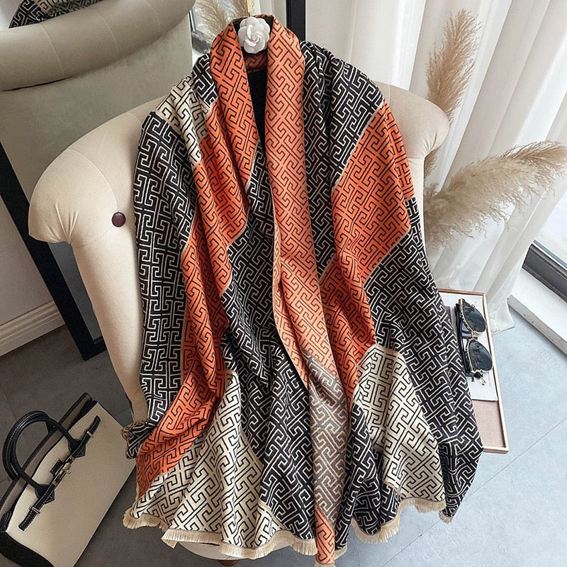 Luxuriöser Schal mit geometrischem Muster in Orange, Schwarz und Beige auf einem Sessel drapiert.