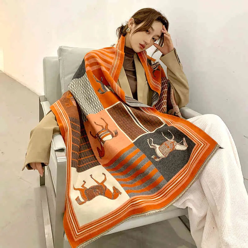 Frau mit orange-grauem Wollschal mit Tiermotiven, sitzt auf einem Sessel, modisch elegant.