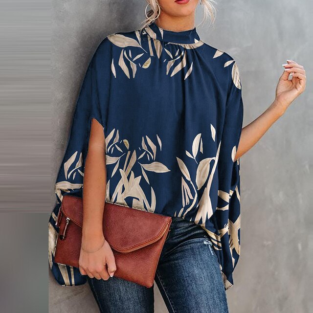 Frau in blauer Batwing-Bluse mit Blattmuster, braune Tasche, lässiger Look.