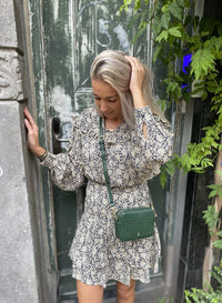 Frau in geblümtem Kleid mit grüner Umhängetasche vor antiker Holztür.