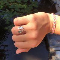 Hand mit silbernem Engelsflügel-Ring und bunter Freundschaftsarmband im Sonnenlicht.