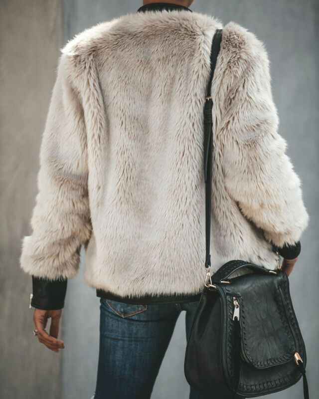 Person in weißer Kunstpelzjacke, blaue Jeans, schwarze Ledertasche, Rückansicht.