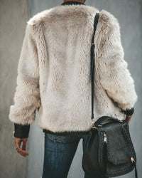 Person in weißer Kunstpelzjacke, blaue Jeans, schwarze Ledertasche, Rückansicht.