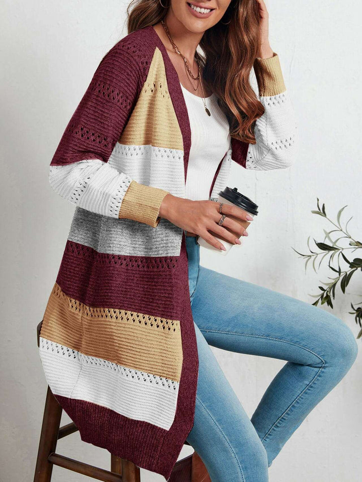 Frau trägt gestreifte Strickweste in Rot, Gelb, Grau und Weiß, kombiniert mit Jeans.