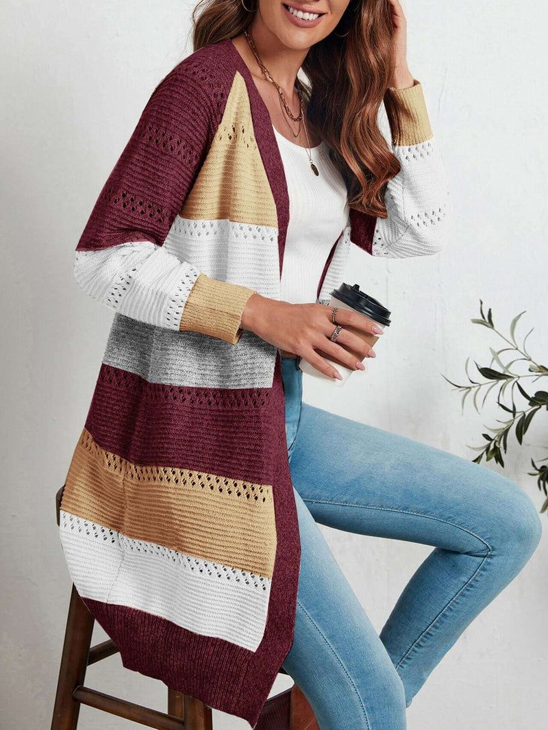 Frau trägt gestreifte Strickweste in Rot, Gelb, Grau und Weiß, kombiniert mit Jeans.