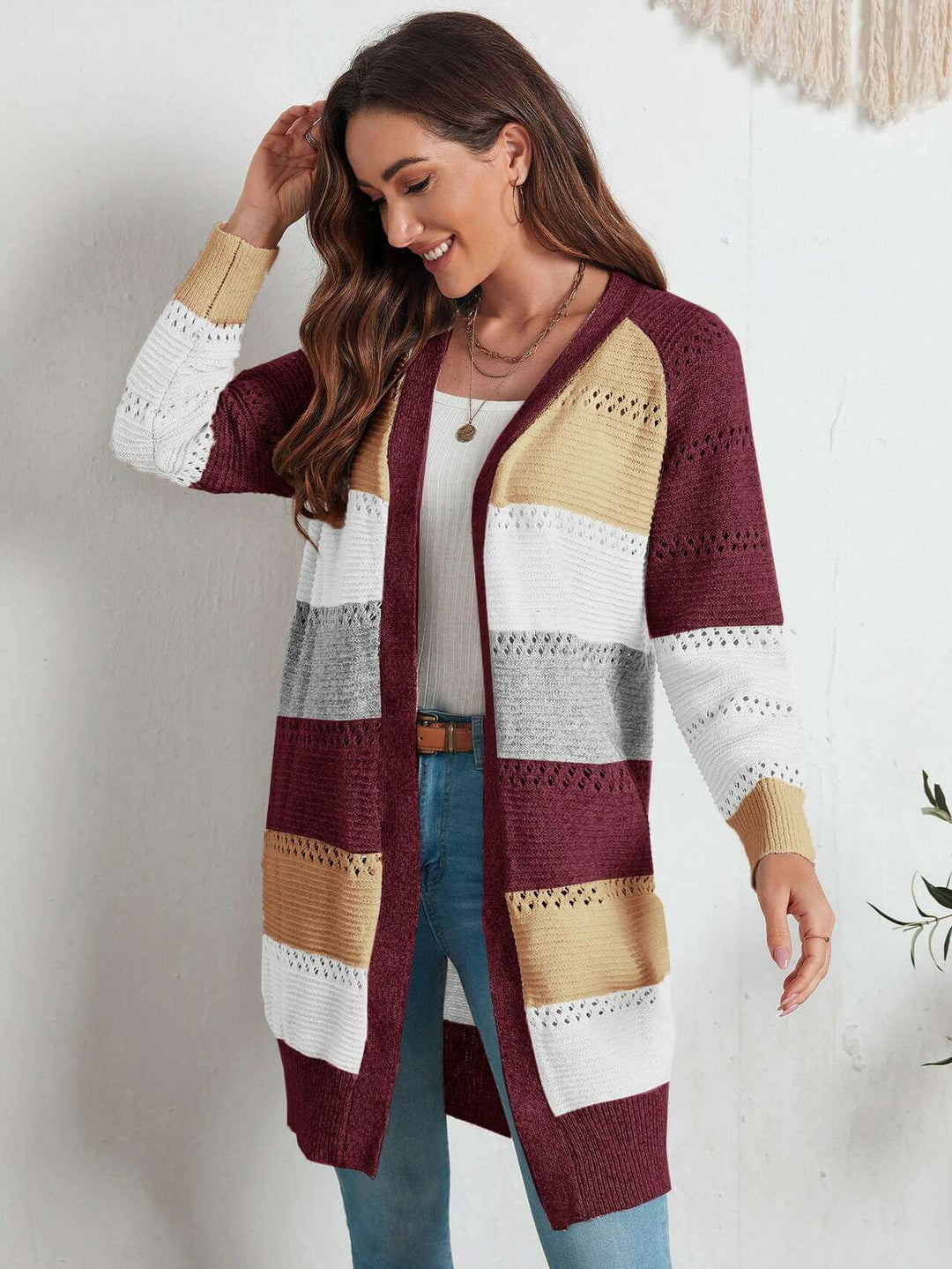 Frau trägt gestreifte Strickweste in Burgunder, Weiß, Grau und Gelb, lässiger Herbstlook.