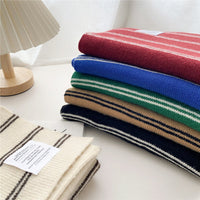 Gestreifte Wollschals in Rot, Blau, Grün, Beige und Schwarz auf einem Tisch.