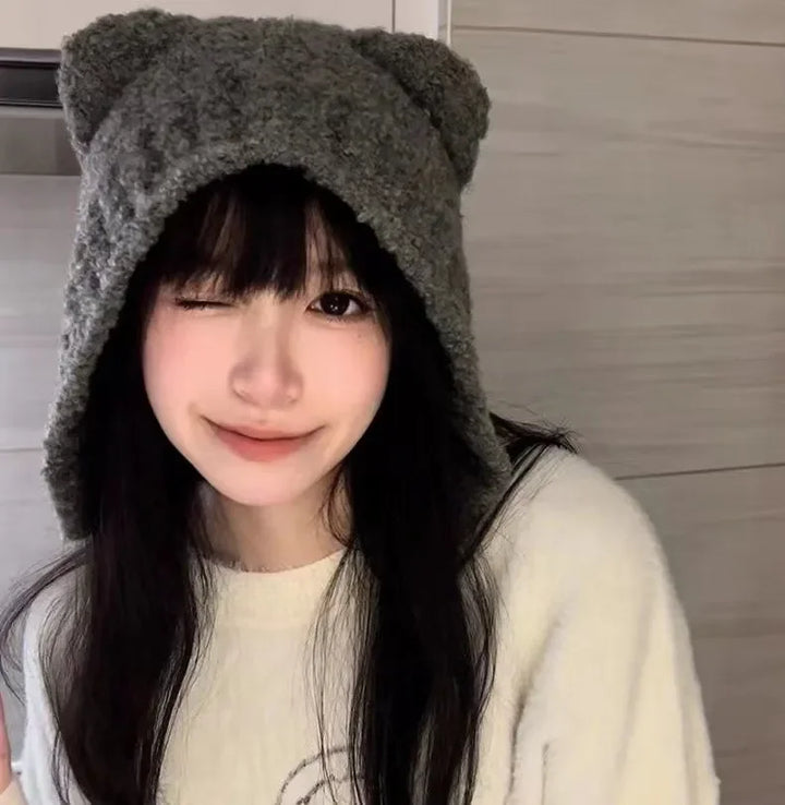 Frau mit grauer Strickmütze mit Katzenohren, lächelnd, in weißem Pullover.