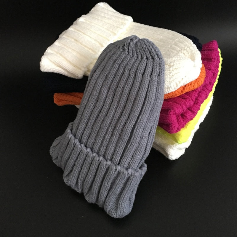 Graue Strickmütze aus Wolle, gestapelt auf bunte Mützen, Wintermode Accessoire.