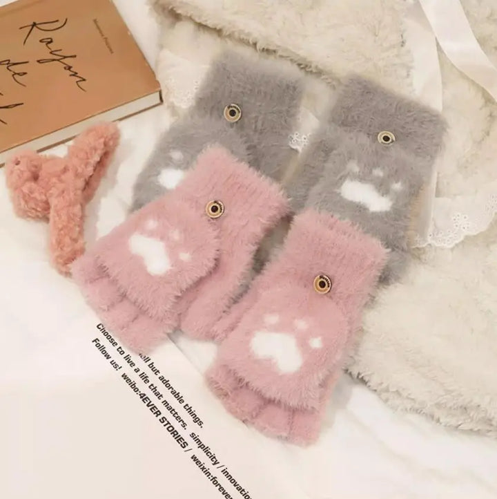 Flauschige rosa und graue Fingerlose Handschuhe mit Pfotenmuster auf weißem Bett.
