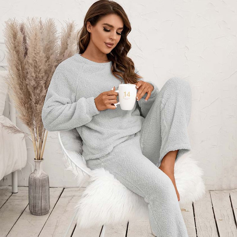 Frau in grauem Fleece-Pyjama mit Tasse, sitzt auf Stuhl, gemütliche Wintermode.