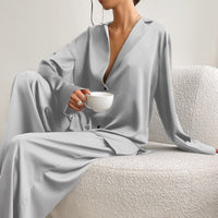 Frau in grauem Satin-Pyjama hält Tasse, sitzt auf weißem Sofa, elegantes Lounge-Outfit.