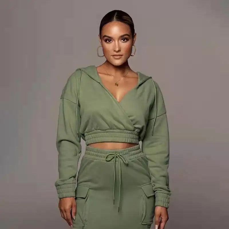 Frau in grünem Kapuzen-Crop-Top und Jogginghose, Freizeitmode, sportlich, modern.