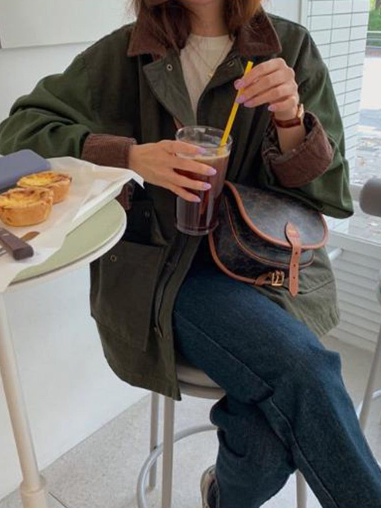 Frau in grüner Jacke mit brauner Tasche, trinkt Eiskaffee, sitzt an Tisch mit Gebäck.