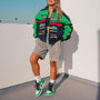 Frau in grüner Rennjacke und gestreiften Shorts, trägt grün-weiße Sneakers, urbaner Stil.