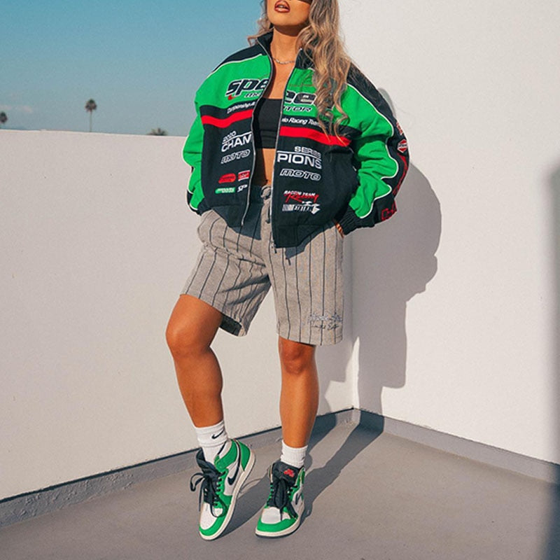 Frau in grüner Rennjacke, gestreifter Shorts und grünen Sneakers auf Balkon.