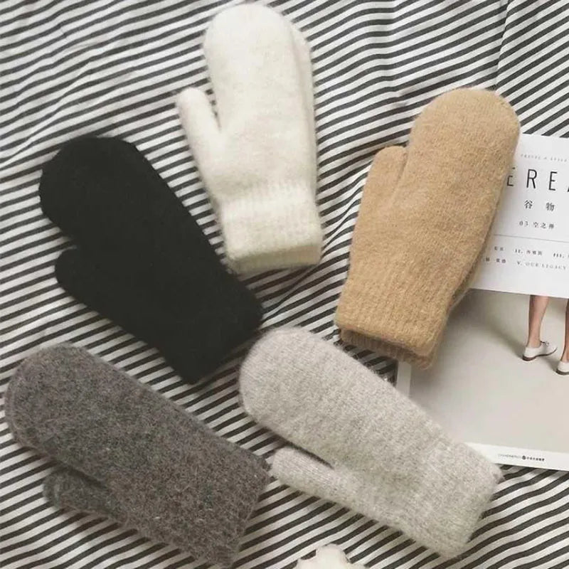 Fünf Paar gestrickte Fäustlinge in Schwarz, Weiß, Beige, Grau auf gestreiftem Hintergrund.