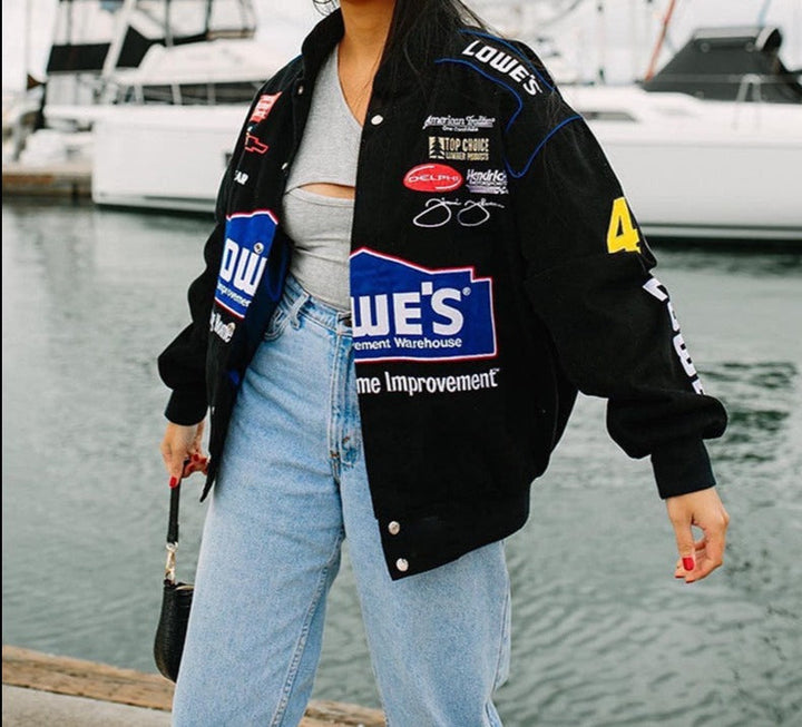 Frau in schwarzer Lowe's Rennjacke, Jeans, Hafenhintergrund, Freizeitmode.