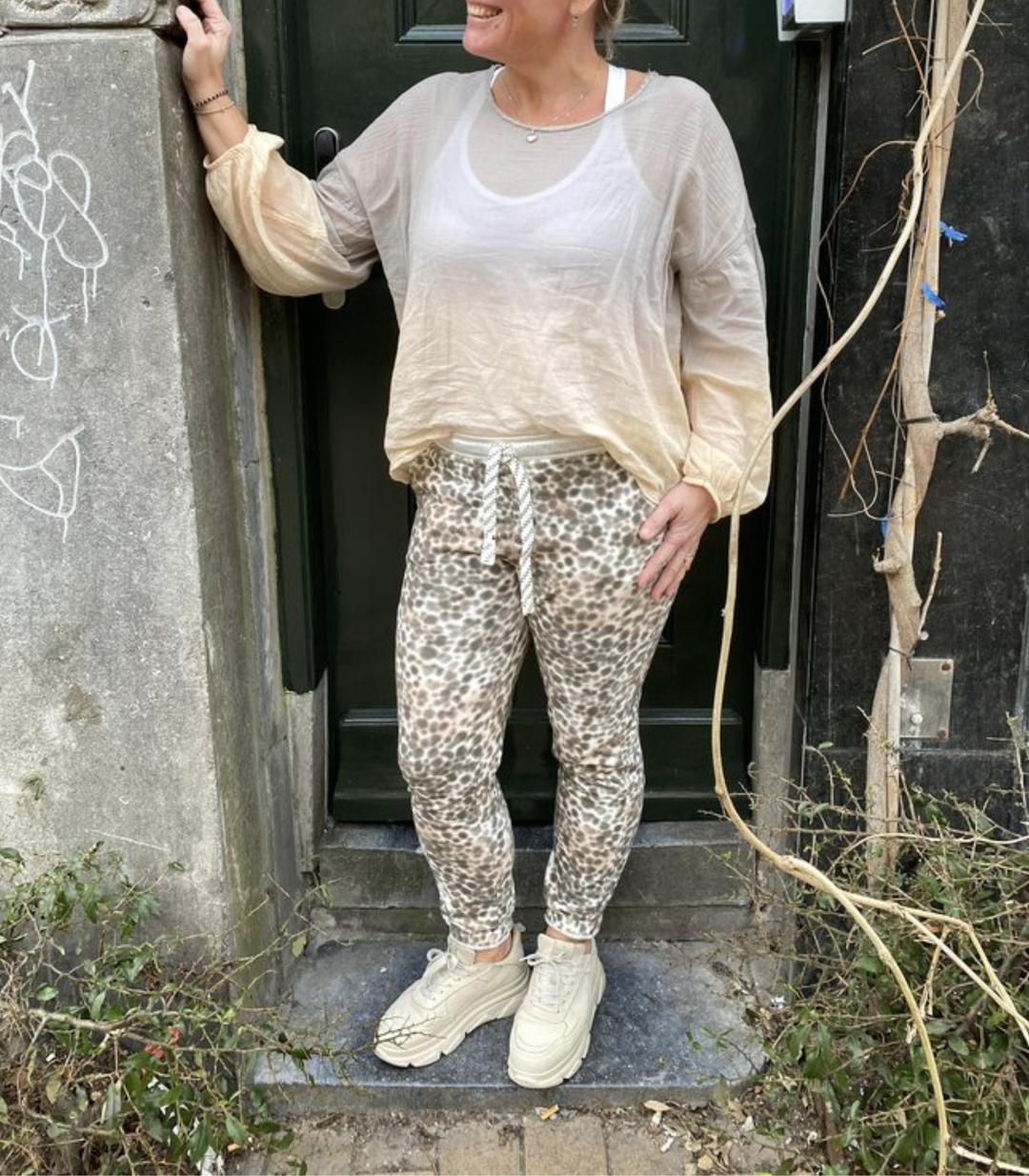 Frau in beiger Bluse und Leopardenhose vor grüner Tür, lässige Mode, Streetstyle.