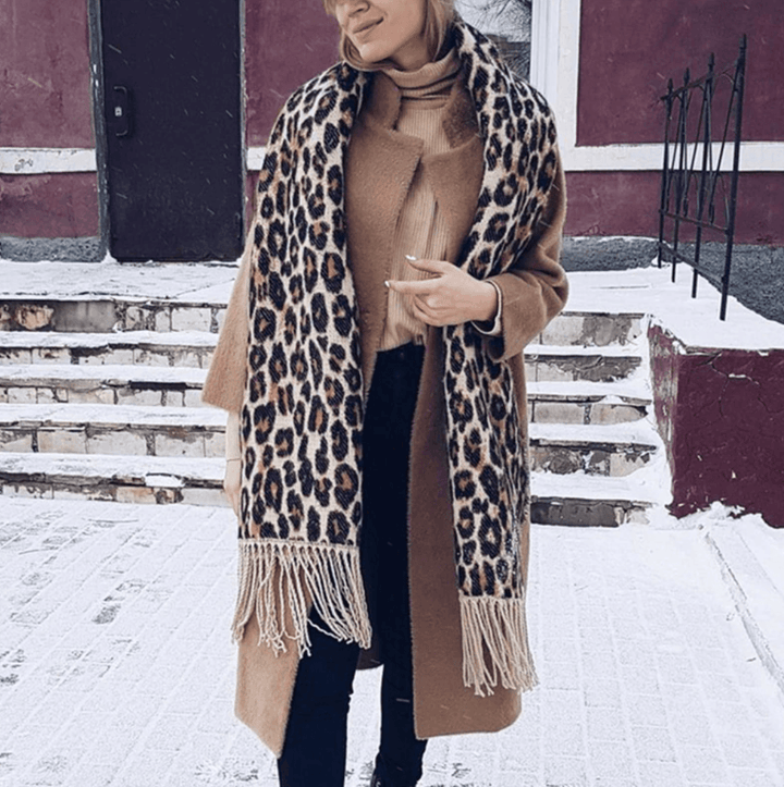 Frau mit Leopardenmuster-Schal und braunem Mantel im Winter auf verschneiter Straße.