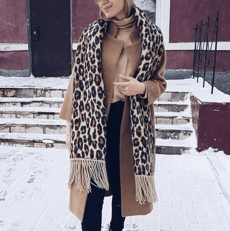 Frau mit Leopardenmuster-Schal und braunem Mantel im Winter auf verschneiter Straße.