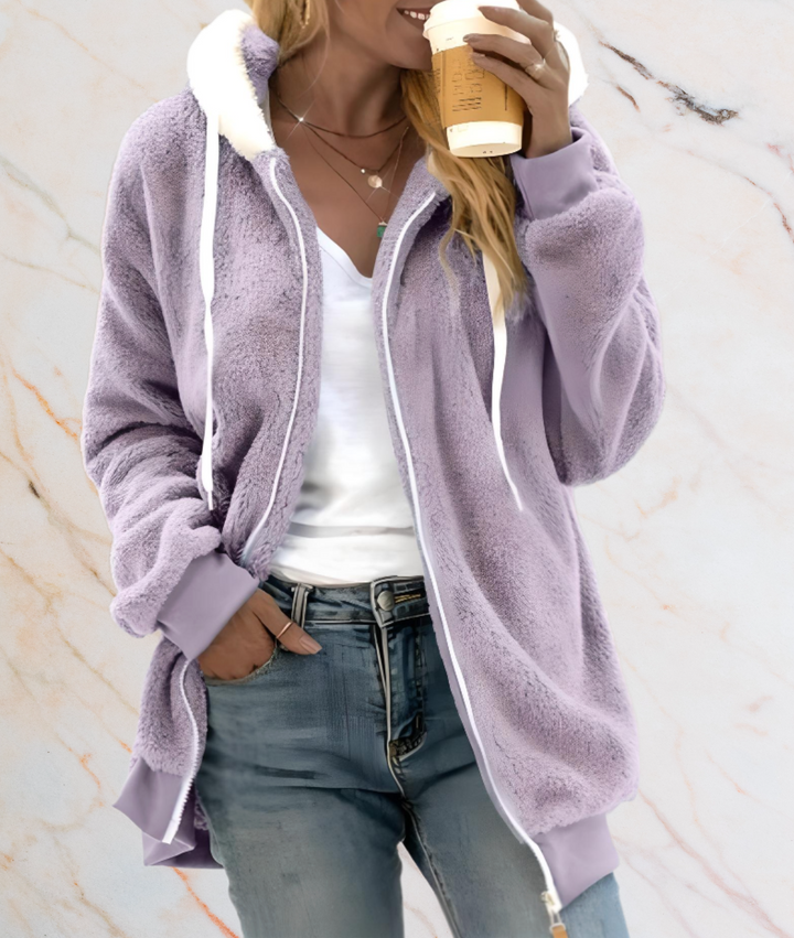 Frau in lila Fleecejacke mit Kapuze, hält Kaffeebecher, lässige Mode, Herbstkleidung.