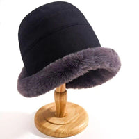 Schwarzer Eimerhut mit grauem Kunstfellrand auf Holzständer, Wintermode Accessoire.