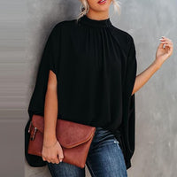 Frau in schwarzer Batwing-Bluse mit brauner Clutch, lässiger Look, Mode für Frühling und Sommer.