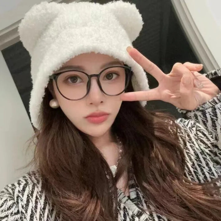 Frau mit weißem Plüsch-Bärenmütze und Brille, zeigt Peace-Zeichen, modisches Winteroutfit.