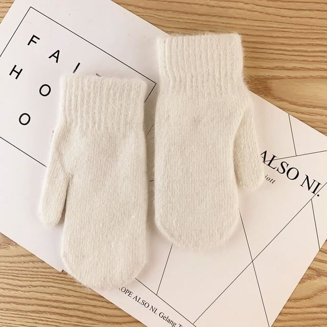 Weiße Wollfäustlinge auf Holztisch, warme Winterhandschuhe, gestrickt, modisch.